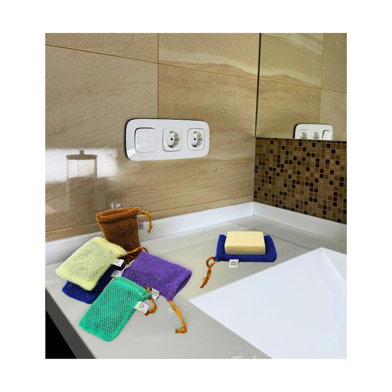 May include: A collection of colorful mesh soap bags in green, blue, yellow, purple, and brown, with a blue soap holder. The bags have drawstring closures and small tags. A bar of soap rests on a blue holder.