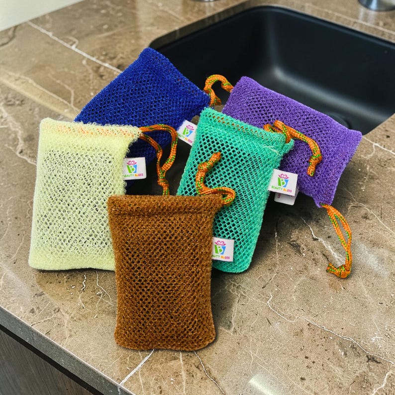 May include: A collection of colorful mesh soap bags in shades of blue, green, purple, yellow, and brown. Each bag has a drawstring closure with an orange and green cord and a small white tag with a logo.