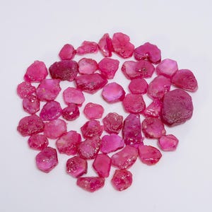 Puede incluir: Una colección de piedras preciosas de rubí rosa sueltas. Los rubíes son de varias formas y tamaños, algunos tienen un acabado más pulido que otros.