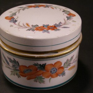 May include: A white porcelain jar with a gold trim and floral designs. The lid has a wreath of flowers and leaves in shades of orange, red, and green.