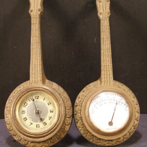 May include: Two antique-style wall clocks shaped like banjos. The clock on the left has a traditional clock face with black hands and Roman numerals. The clock on the right has a round thermometer face with a black needle and a white background. Both clocks have a gold finish and intricate details.