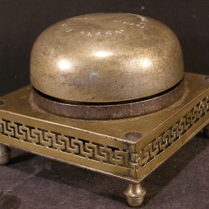 May include: A brass bell with a decorative base, the bell is inscribed with the words "The Improved Alarm".