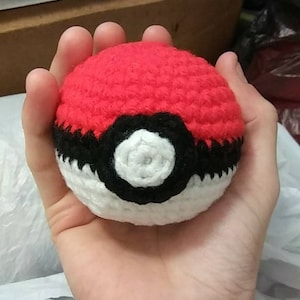 May include: A red, white, and black crocheted Poké Ball. The Poké Ball is a popular item from the Pokémon franchise.