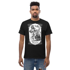 Könnte beinhalten: Schwarzes T-Shirt mit einem weißen Grafikdruck eines Dämons mit Hörnern und einem Schwanz. Der Dämon hält einen Stab und ist von einem dekorativen Rahmen umgeben. Der Text "Azazel" ist unter dem Dämon gedruckt.