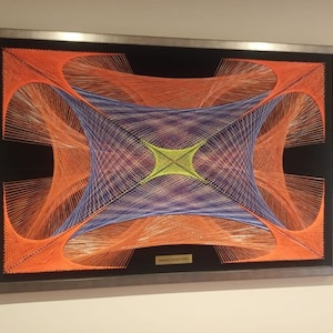 May include: A framed string art piece with a geometric design. The artwork features orange, blue, and green threads on a black background.
