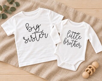 May include: A white short-sleeved t-shirt with the black text big sister and a white long-sleeved bodysuit with the black text little brother. Both garments feature a simple crew neckline and are made of a plain white fabric.