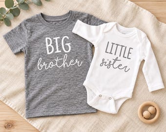 May include: A charcoal gray short-sleeve t-shirt with the white text BIG brother and a white long-sleeve bodysuit with the gray text LITTLE sister. The t-shirt features a crew neckline and the bodysuit has a snap closure at the bottom.