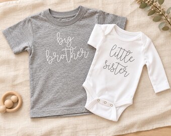 May include: A heather gray short-sleeve t-shirt with the white text big brother and a white long-sleeve bodysuit with the dark gray text little sister. The bodysuit features three metal snaps at the bottom for closure and a round neckline.