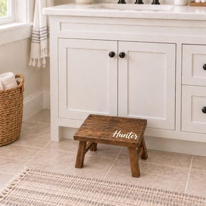 May include: A small, rectangular wooden step stool with a dark brown stained finish. The top surface of the stool features the name Hunter written in white script lettering. The stool has four sturdy legs and a simple, functional design.