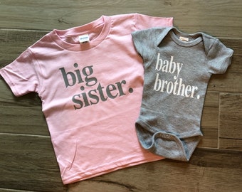 May include: Pink and gray t-shirts with the text "big sister." and "baby brother." printed on them.