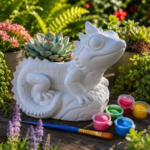 May include: A white lizard-shaped planter with a textured surface and a hollow back for a succulent. The set includes a blue-handled paintbrush and five small plastic pots containing pink, green, yellow, and blue paint for decorating the figure.
