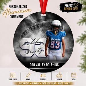 Puede incluir: Un adorno redondo de aluminio que muestra a un jugador de fútbol americano con uniforme azul y blanco con el número 93. El diseño incluye un gráfico de un balón de fútbol, el texto Nikolas Christy y el nombre Oro Valley Dolphins.