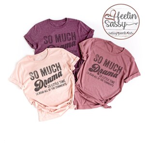 May include: Three t-shirts in shades of pink and purple, each with the phrase "SO MUCH Drama, SO LITTLE TIME TO READ ALL OF THE COMMENTS" printed in distressed black lettering. A circular logo with the text "Feelin Sassy" is in the upper right corner.