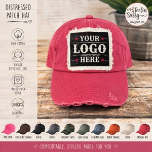 May include: A bright pink baseball cap with a distressed, frayed-edge rectangular patch on the front. The patch is black with white text that reads YOUR LOGO HERE, accented by two small red stars. The cap features a worn, vintage-style finish.