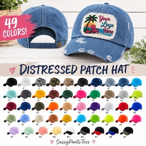 May include: A blue denim baseball cap with a distressed finish and a rectangular patch featuring a tropical beach scene with a palm tree, a red chair, and the text Your Logo Here. The cap has a curved brim and an adjustable back strap.