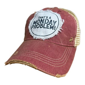 May include: A red and tan distressed trucker hat with a white patch that says "That's a Monday Problem!" in black text.