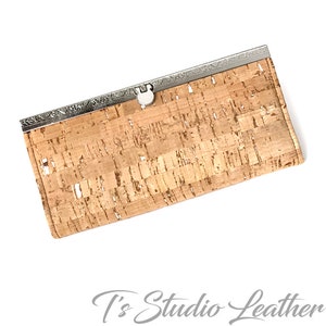 May include: A brown cork wallet with a silver metal clasp and a decorative border. The wallet is made of natural cork and has a textured surface.
