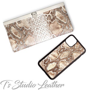 Może przedstawiać: Brązowy i biały portfel ze sk&oacute;ry węża z srebrnym zapięciem i pasujące etui na telefon ze sk&oacute;ry węża w kolorze brązowym i białym.