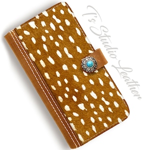 May include: A brown leather wallet with a white spotted pattern. The wallet has a flap closure with a silver and turquoise stone embellishment. It's Studio Leather.