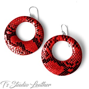 May include: A pair of red hoop earrings with a snakeskin pattern. The earrings are made of leather and have a silver hook closure.