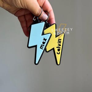 May include: Two lightning bolt shaped keychains with black outlines. One is blue with the name "max" written on it and the other is yellow with the name "calvin" written on it.