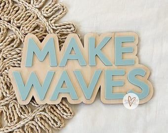 May include: Wooden sign with the text "MAKE WAVES" in light blue letters. The sign is on a woven straw background.