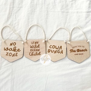 May include: Four wooden signs with rope hangers and various phrases, including "No Wake Zone", "Stay Wild Ocean Child", "Cowa Bunga", and "Love You to the Beach and Back".