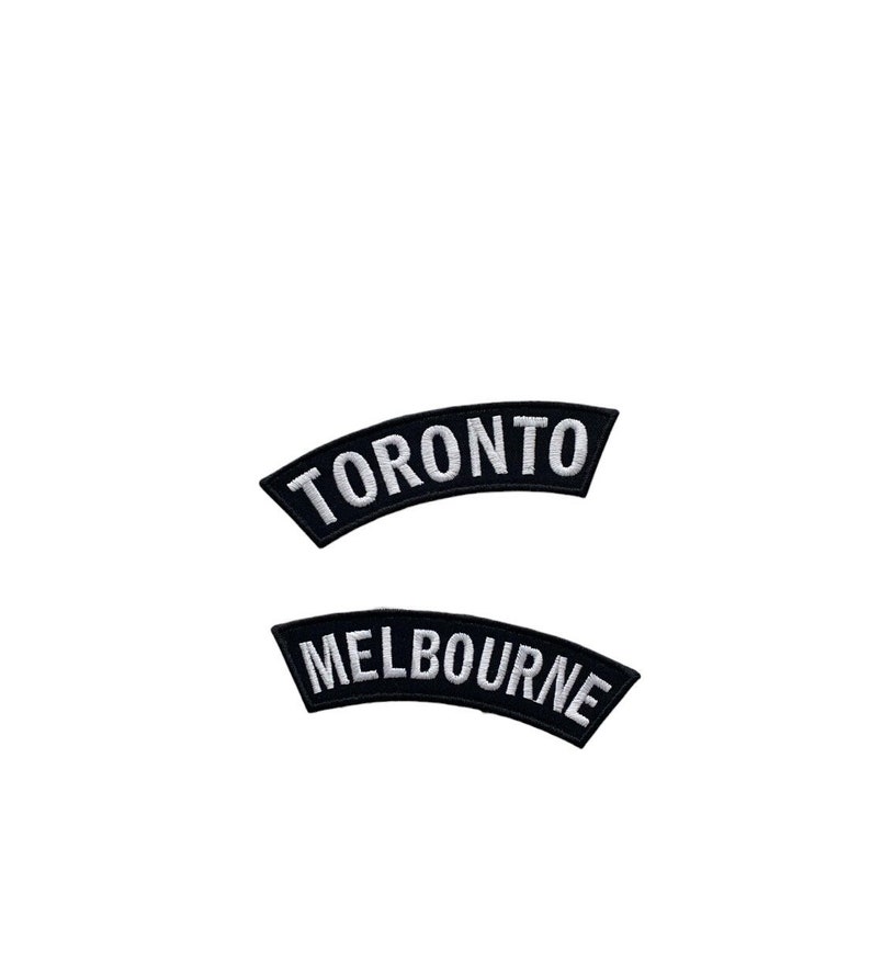 May include: Two black embroidered patches with white text. The top patch reads "TORONTO" in a curved design. The bottom patch reads "MELBOURNE" in a similar curved design. Both patches are isolated on a white background.