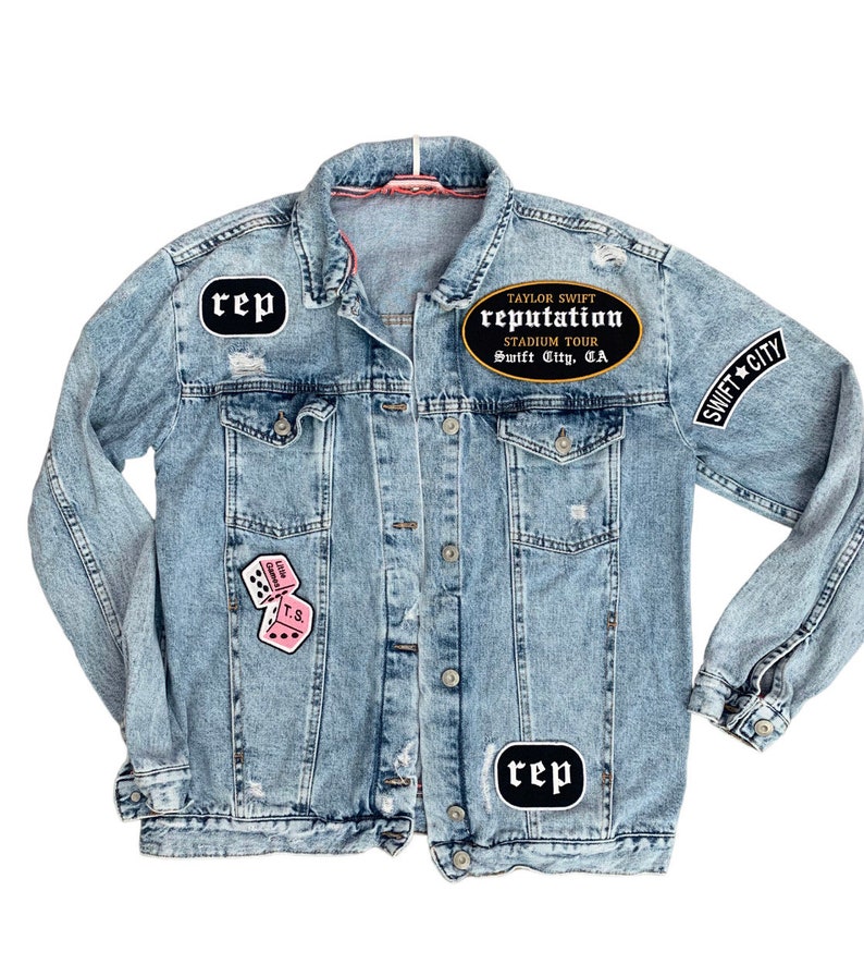 May include: Light blue denim jacket with various patches. Patches include the word "rep" in a black oval, pink dice, and a black oval patch that reads "Taylor Swift Reputation Stadium Tour Swift City, CA" and "Swift City".