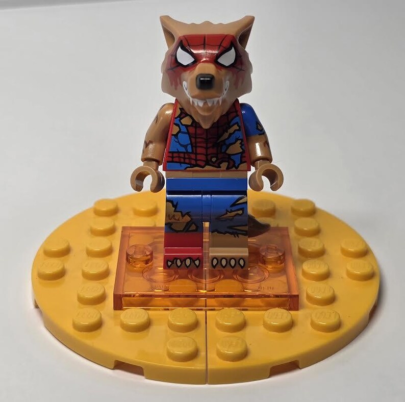 May include: A Lego minifigure of a werewolf character, with a brown wolf head and a torn Spider-Man costume. The figure stands on a yellow Lego base with a clear orange platform.