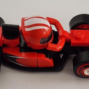 May include: A red and black Lego Ferrari race car with a white stripe on the helmet. The car has the word "Ferrari" printed on the back.