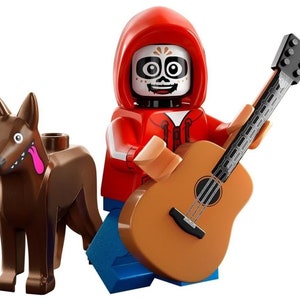 Puede incluir: Una minifigura LEGO de un esqueleto que lleva una sudadera con capucha roja y pantalones vaqueros azules, tocando una guitarra acústica marrón. La minifigura tiene una cara pintada con un diseño de calavera y una lengua rosa que sobresale. Un perro marrón con una lengua rosa está de pie junto a la minifigura.