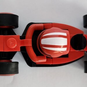 May include: A red toy race car with black wheels and a white stripe on the helmet. The car has a "Ferrari" logo on the side and a "Lego" logo on the bottom.