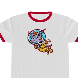 May include: White t-shirt with a red trim around the collar and sleeves. The shirt features a cartoon illustration of a purple cat in a space suit. The cat is floating in space with a blue bubble helmet.