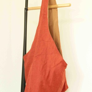 May include: A hobo-style shoulder bag featuring a vibrant rust-orange exterior and a contrasting tan interior lining. The bag has a single integrated strap design that forms a continuous loop, creating a soft, unstructured silhouette for carrying.