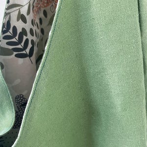 May include: A sage green tote bag with a textured fabric exterior and a contrasting interior lining featuring a botanical print of leaves, stems, and abstract shapes in shades of dark green, light green, and muted orange on a cream background.