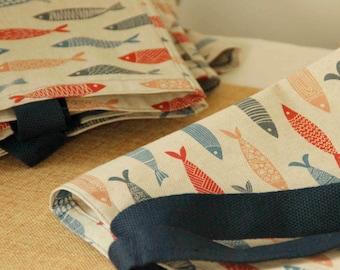 May include: A beige fabric tote bag featuring a repeating pattern of stylized fish in shades of red, orange, and blue. The bag includes sturdy dark navy blue woven handles and is constructed from a textured, natural-colored textile material.