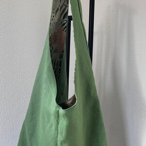 May include: A solid sage green hobo bag with a single wide shoulder strap. The interior lining features a contrasting pattern of dark brown and cream botanical leaf illustrations, visible along the inner edge and the top opening of the bag.