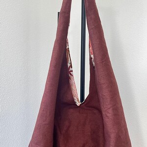 May include: A deep maroon hobo bag featuring a wide shoulder strap and a contrasting interior lining. The interior fabric displays a multi-colored floral and leaf pattern in shades of orange, white, and brown against a light background.