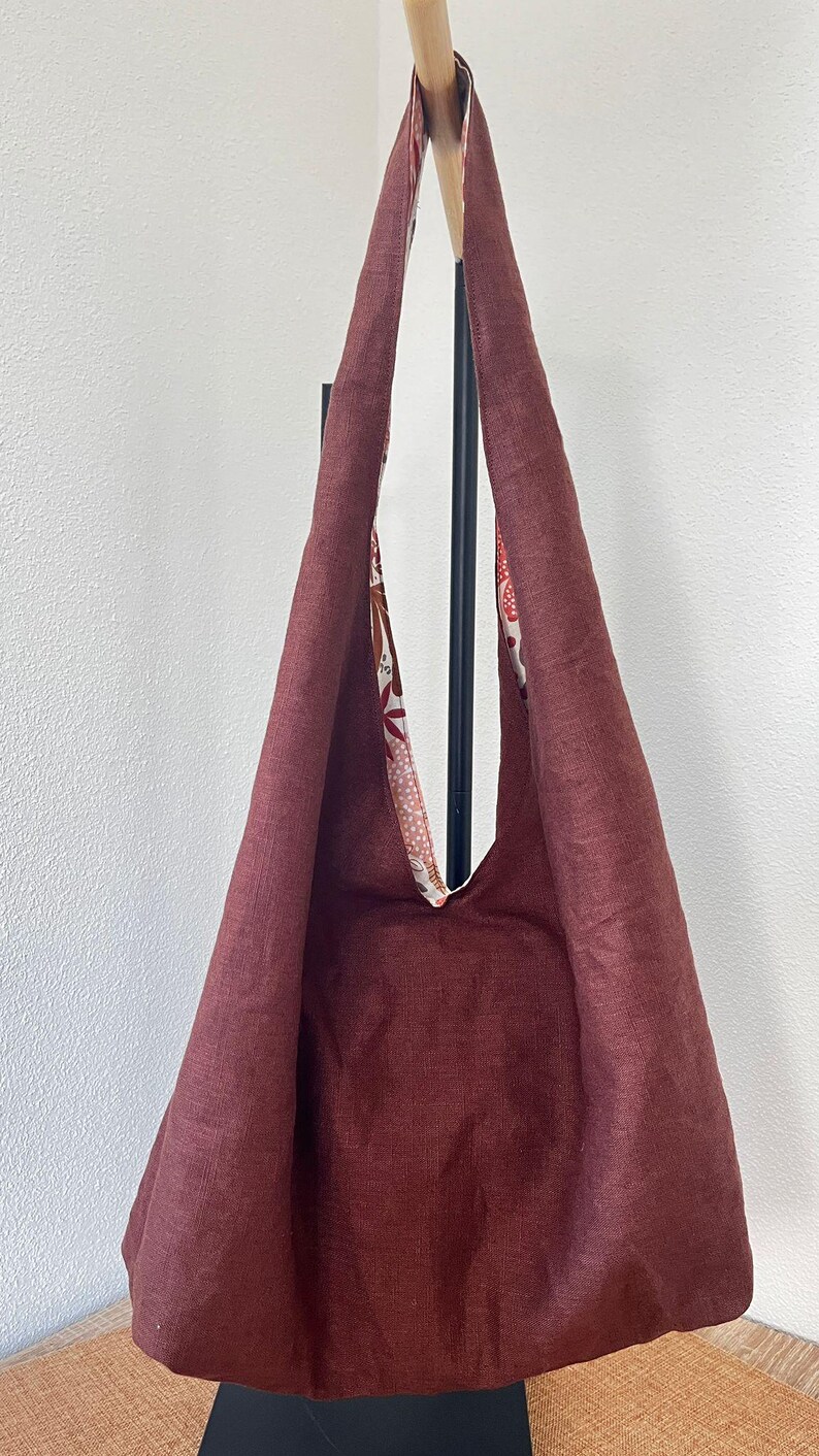 May include: A deep maroon hobo bag featuring a wide shoulder strap and a contrasting interior lining. The interior fabric displays a multi-colored floral and leaf pattern in shades of orange, white, and brown against a light background.