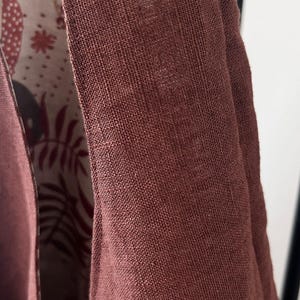 May include: A garment featuring a solid, textured, dark reddish-brown exterior fabric with visible weave. The interior lining displays a contrasting off-white background patterned with dark brown and reddish-brown botanical leaf illustrations.