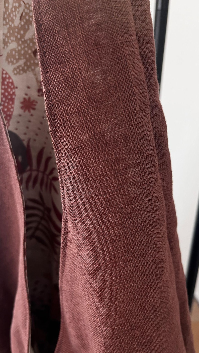 May include: A garment featuring a solid, textured, dark reddish-brown exterior fabric with visible weave. The interior lining displays a contrasting off-white background patterned with dark brown and reddish-brown botanical leaf illustrations.
