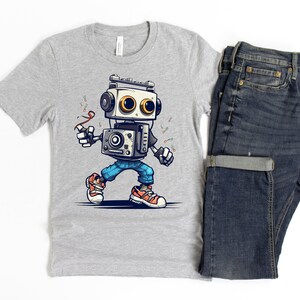 Może przedstawiać: Szary T-shirt z kresk&oacute;wkowym robotem w niebieskich dżinsach i pomarańczowych butach. Robot trzyma czerwoną wstążkę i ma retro styl.