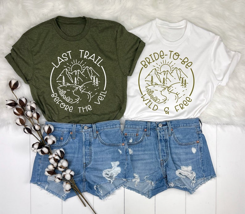 May include: Two t-shirts featuring a mountain scene and text. The green shirt reads "Last Trail Before The Veil" and the white shirt reads "Bride-To-Be Wild & Free".