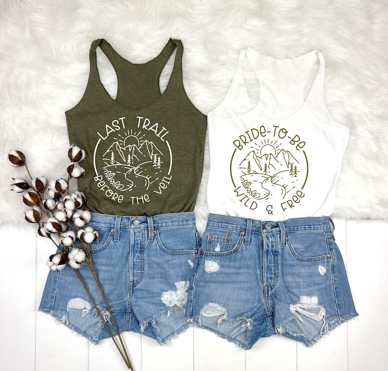 May include: Two tank tops featuring a mountain scene and text. The green tank top reads "Last Trail Before The Veil" and the white tank top reads "Bride-To-Be Wild & Free".