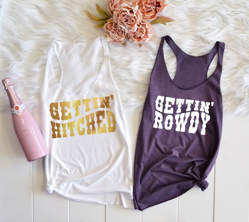 May include: Two white tank tops with gold and white text. The top on the left says "Gettin' Hitched" and the top on the right says "Gettin' Rowdy".