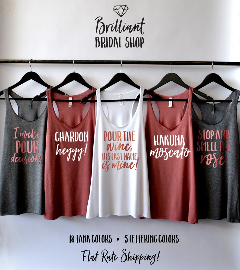 Puede incluir: Cinco camisetas de tirantes con diferentes lemas impresos en ellas. Los lemas son "I make pour decisions", "Chardon heyyy!", "Pour the wine, his last name is mine!", "Hakuna moscato" y "Stop and smell the rose".
