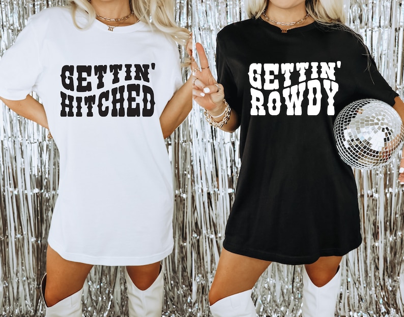 May include: Two women wearing oversized t-shirts. The white shirt says "Gettin' Hitched" and the black shirt says "Gettin' Rowdy".