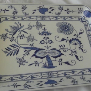 Puede incluir: Bandeja rectangular con fondo blanco y diseño floral azul. La bandeja presenta un borde detallado y motivos florales centrales. La combinación de colores azul y blanco le da un aspecto clásico y elegante.