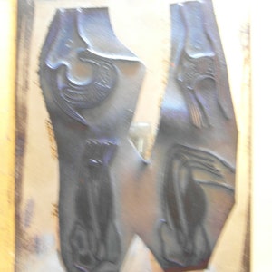 Puede incluir: Dos bloques de impresi&oacute;n azul oscuro con dise&ntilde;os en relieve. Un bloque presenta un perro sentado, el otro un p&aacute;jaro y una articulaci&oacute;n de la rodilla humana. Los bloques est&aacute;n sobre una superficie marr&oacute;n claro.